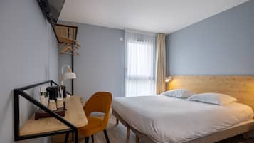 Quarto de hotel com cama, escrivaninha, cadeira, espelho e janela com cortinas.