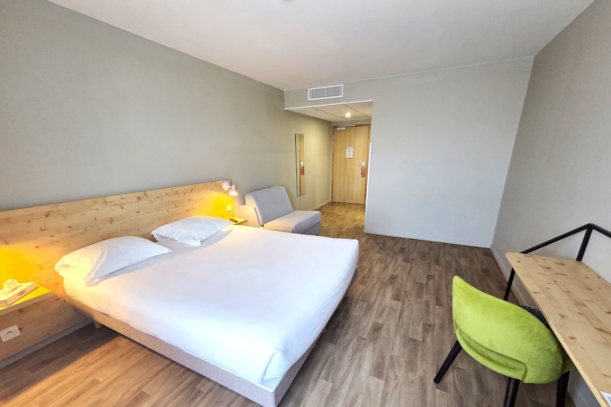 A hotel room with a large bed, a desk, a chair, and a wooden floor.