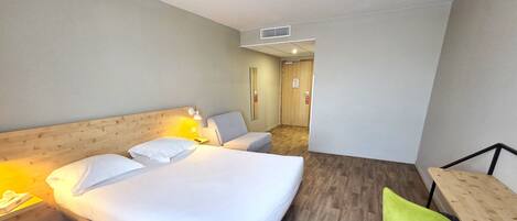 Een hotelkamer met een groot bed, een bureau, een stoel en een houten vloer.