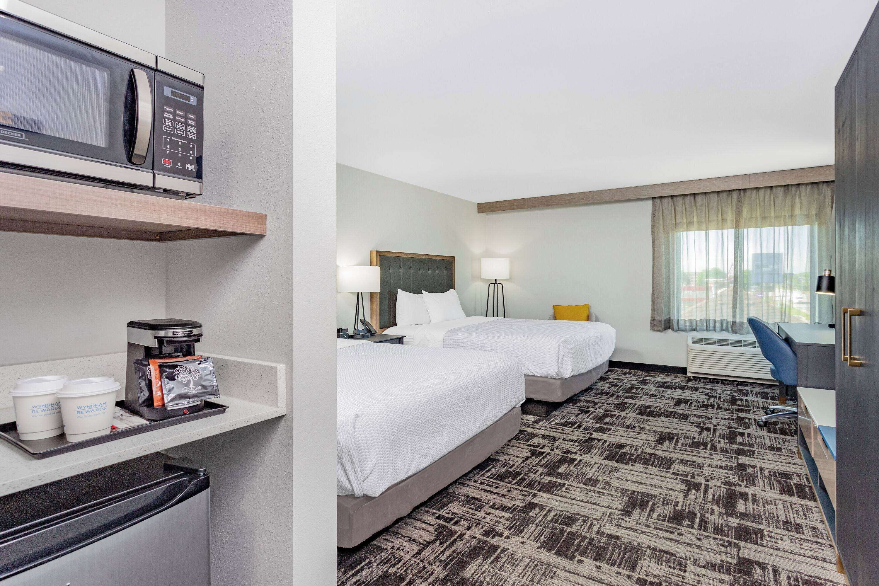 A hotel room with two beds, a microwave, a coffee maker, and a desk with a chair.
