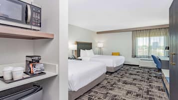 A hotel room with two beds, a microwave, a coffee maker, and a desk with a chair.