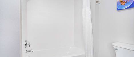 A bathroom with a white bathtub, a toilet, and a shower curtain.