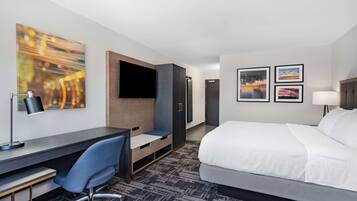 A hotel room with a bed, desk, chair, TV, wardrobe, and artwork on the walls.