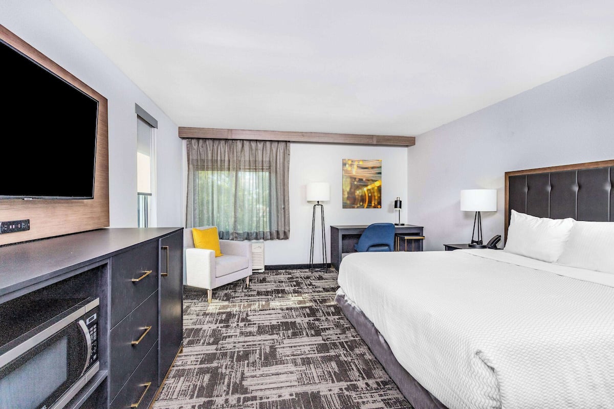Ein Hotelzimmer mit einem großen Bett, einem Flachbildfernseher, einem Schreibtisch mit Stuhl, einer Couch und einer Schreibtischlampe.