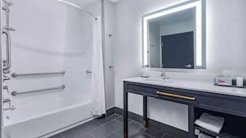 A modern bathroom with a white bathtub, a vanity with a mirror, and a towel rack.