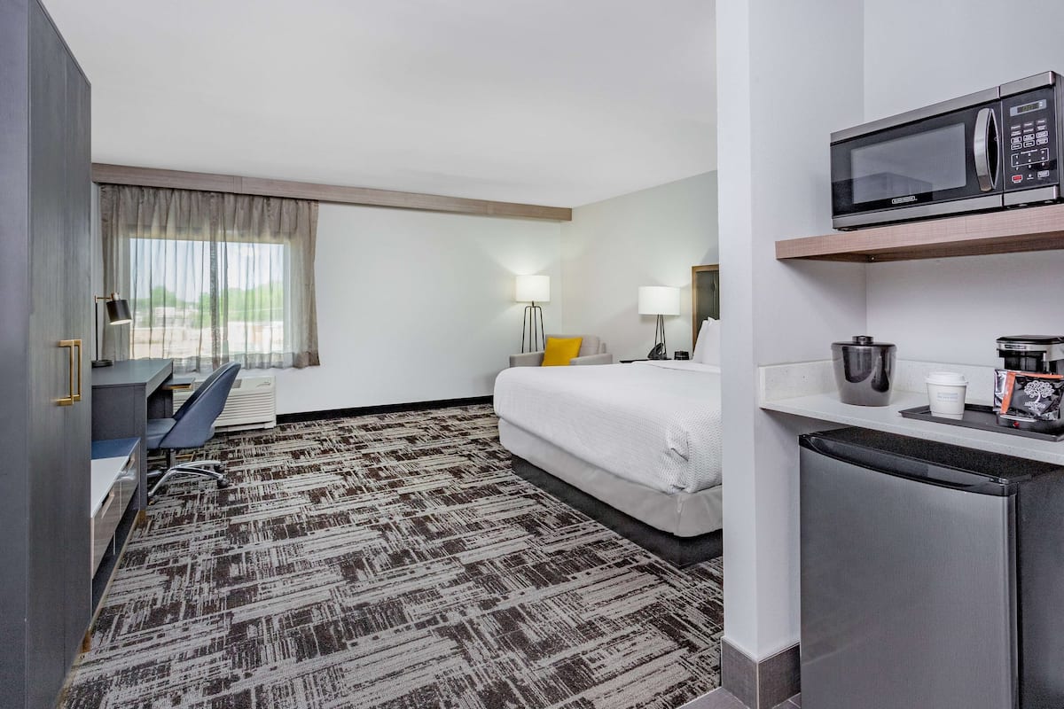 Ein Hotelzimmer mit Bett, Schreibtisch, Stuhl, Mikrowelle und Kühlschrank.