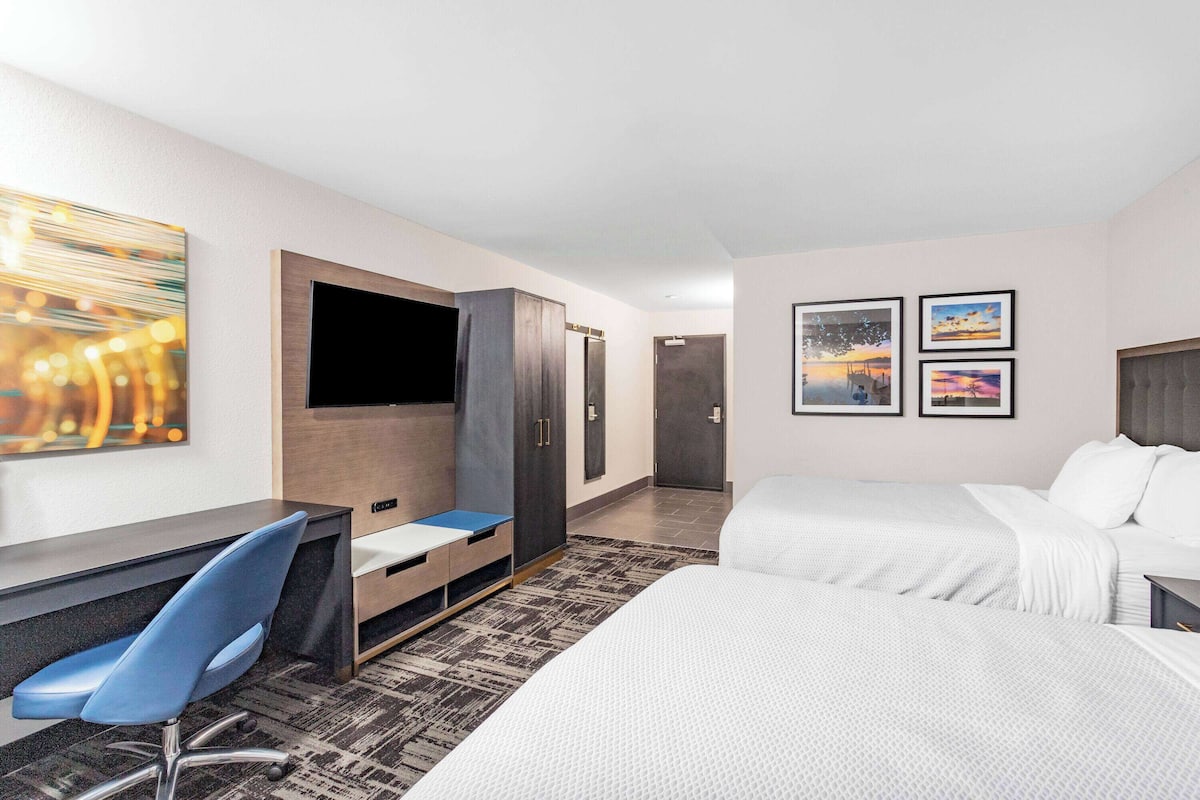 Ein Hotelzimmer mit einem Bett, einem Schreibtisch, einem Sessel, einem Fernseher und Kunstwerken an den Wänden.
