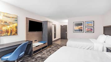A hotel room with a bed, a desk, a chair, a TV, and artwork on the walls.