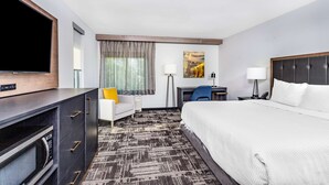Habitación de hotel con una cama grande, un escritorio, una silla, un televisor y un microondas.