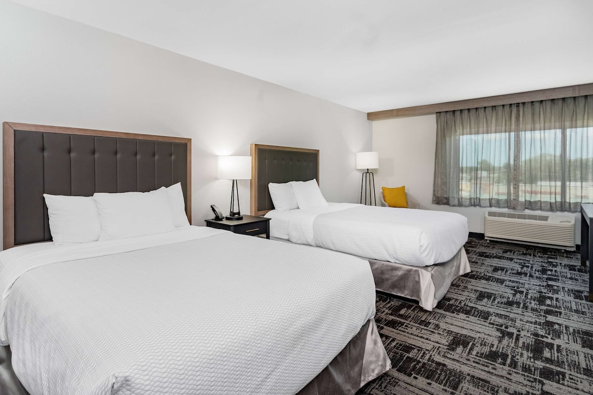 Ein Hotelzimmer mit zwei Betten, einem Schreibtisch, einem Sessel und einem großen Fenster mit Vorhängen.