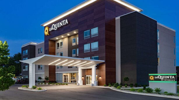 Un hotel moderno con un llamativo letrero de 'La Quinta by Wyndham', que presenta una estructura de varios pisos con un acceso cubierto y una fachada bien iluminada.