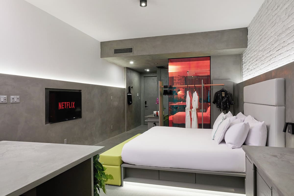 Un dormitorio moderno con cama, televisor montado en la pared y armario con iluminación roja.