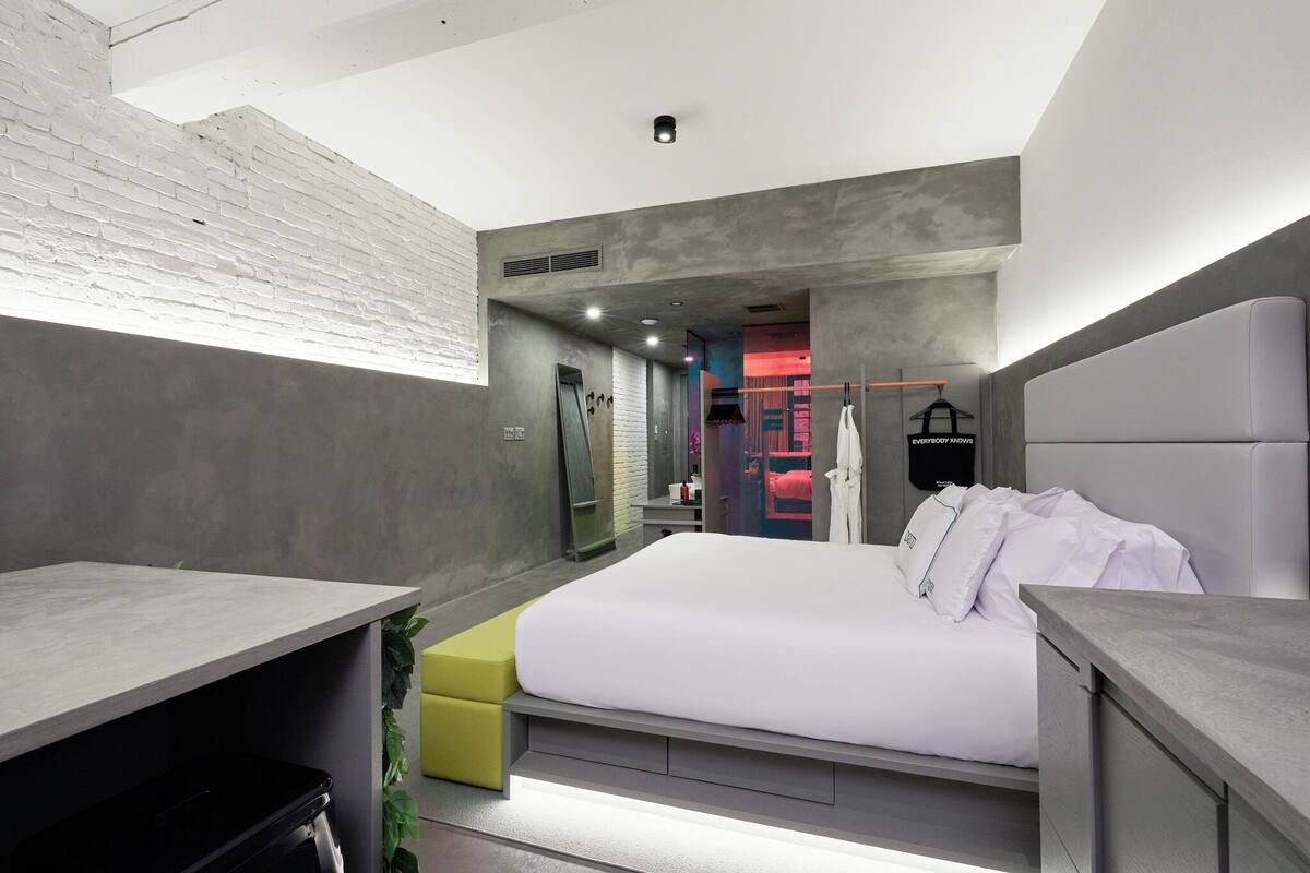 Un dormitorio moderno con una cama grande, una mesita de noche, un taburete pequeño y un armario.
