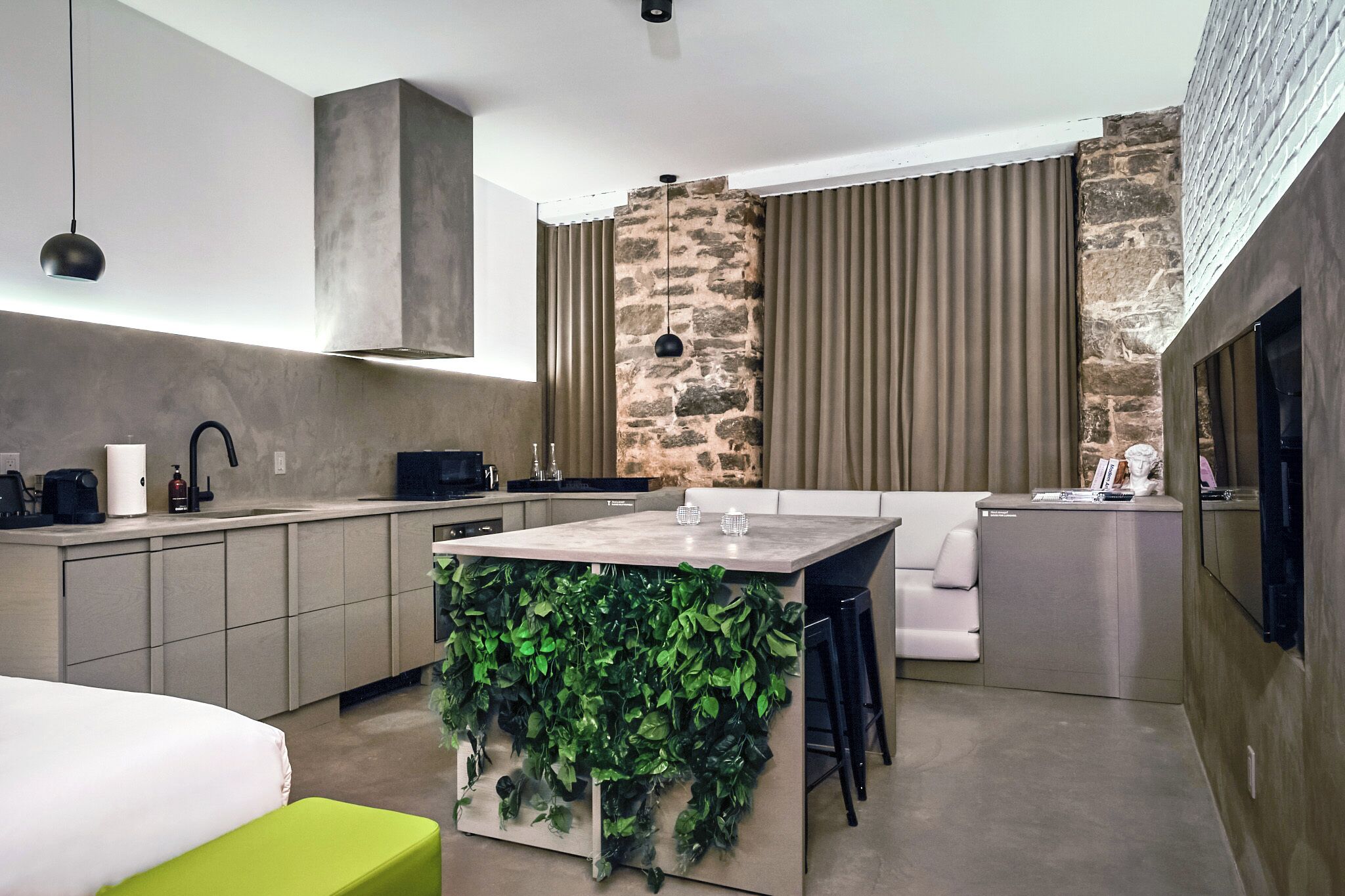 A modern kitchen with a stone accent wall, a central island with greenery, and a dining area with a sofa.