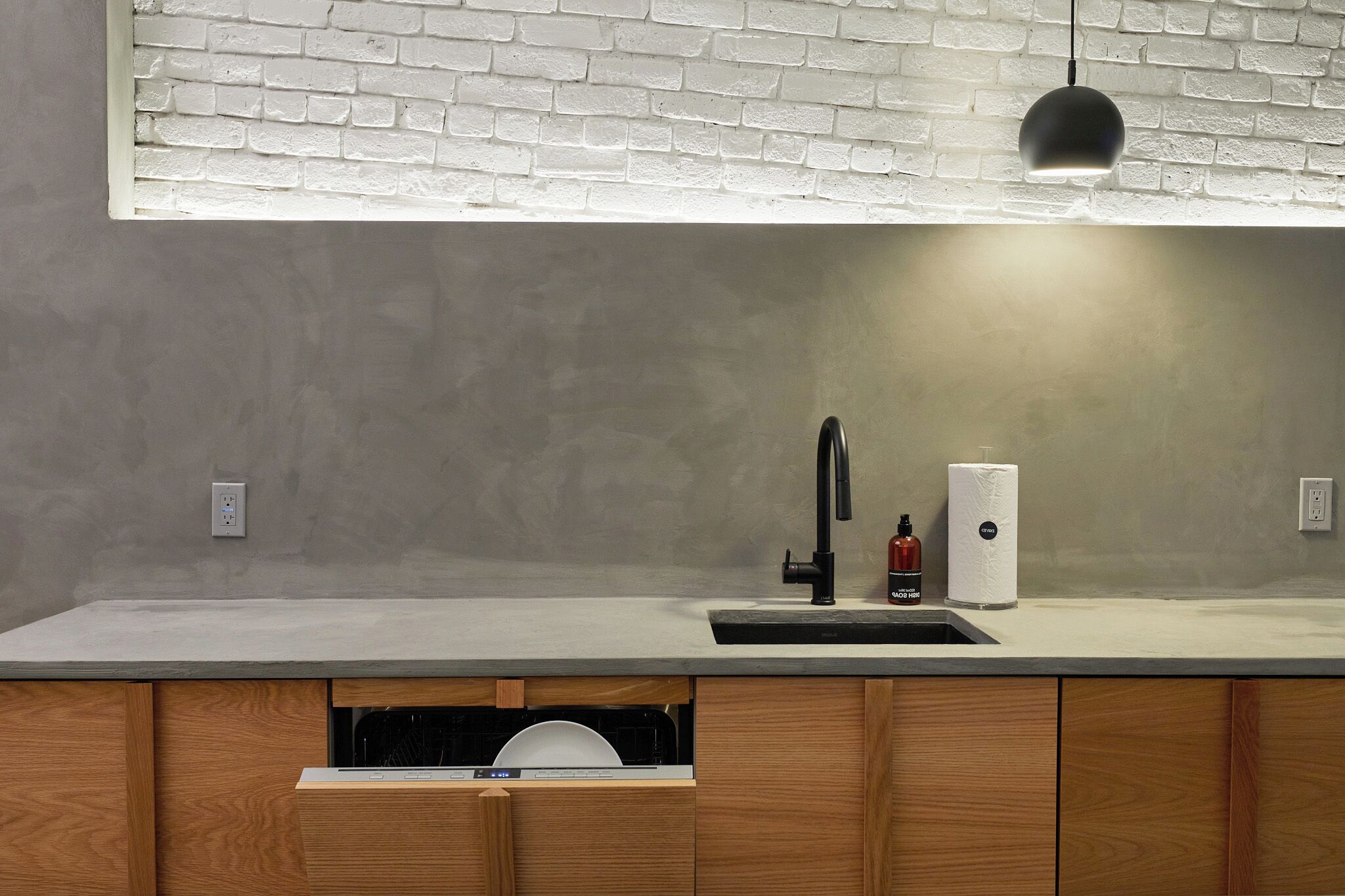 A modern kitchen with a white brick backsplash, a black faucet, and a built-in dishwasher.