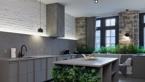 A modern kitchen with grey cabinets, a central island with greenery, a stone accent wall, and a large window with curtains. - David Hotel (Montreal)