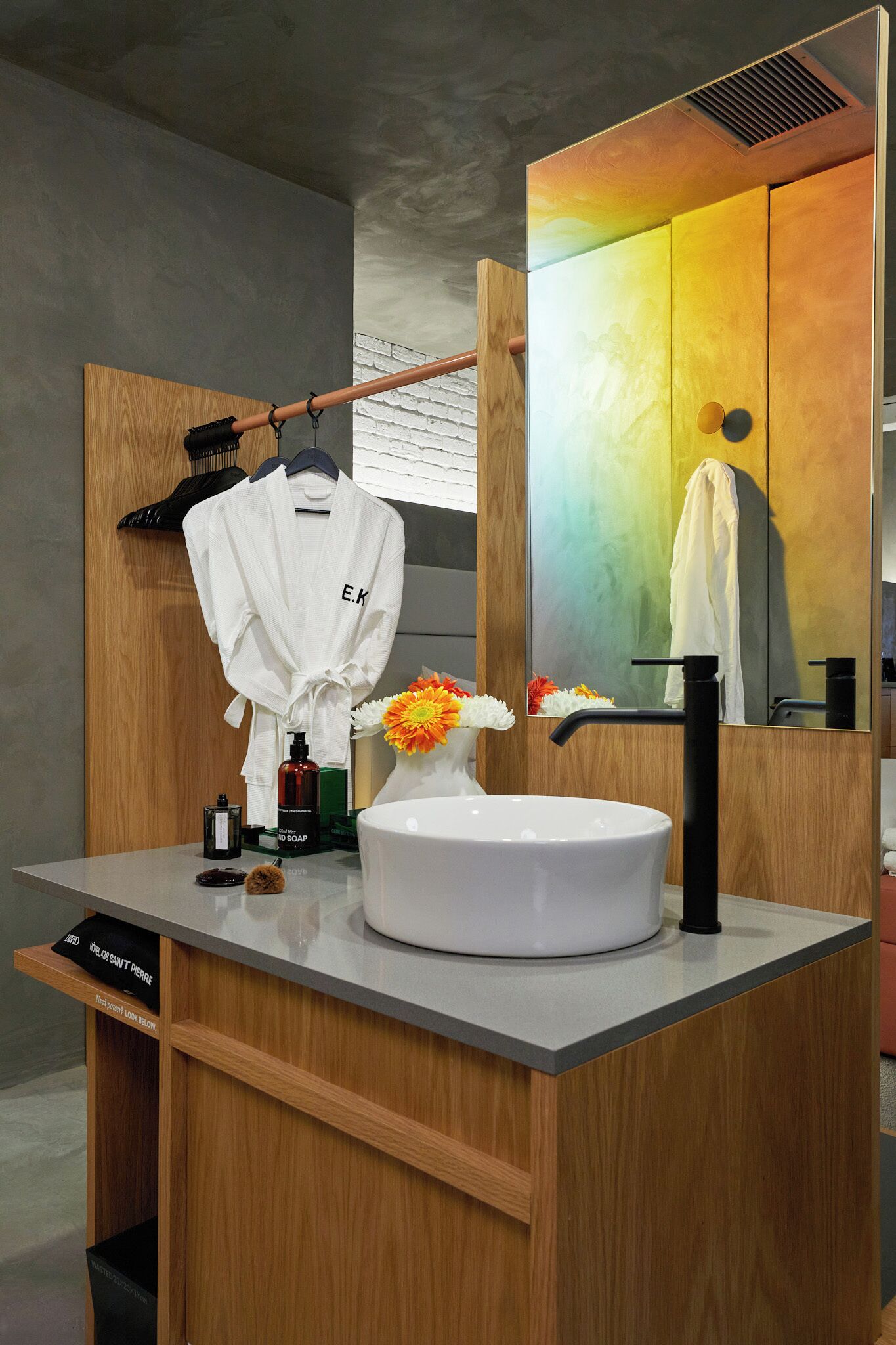 A modern bathroom with a wooden vanity, a white sink, a mirror, and a robe hanging on a rack.