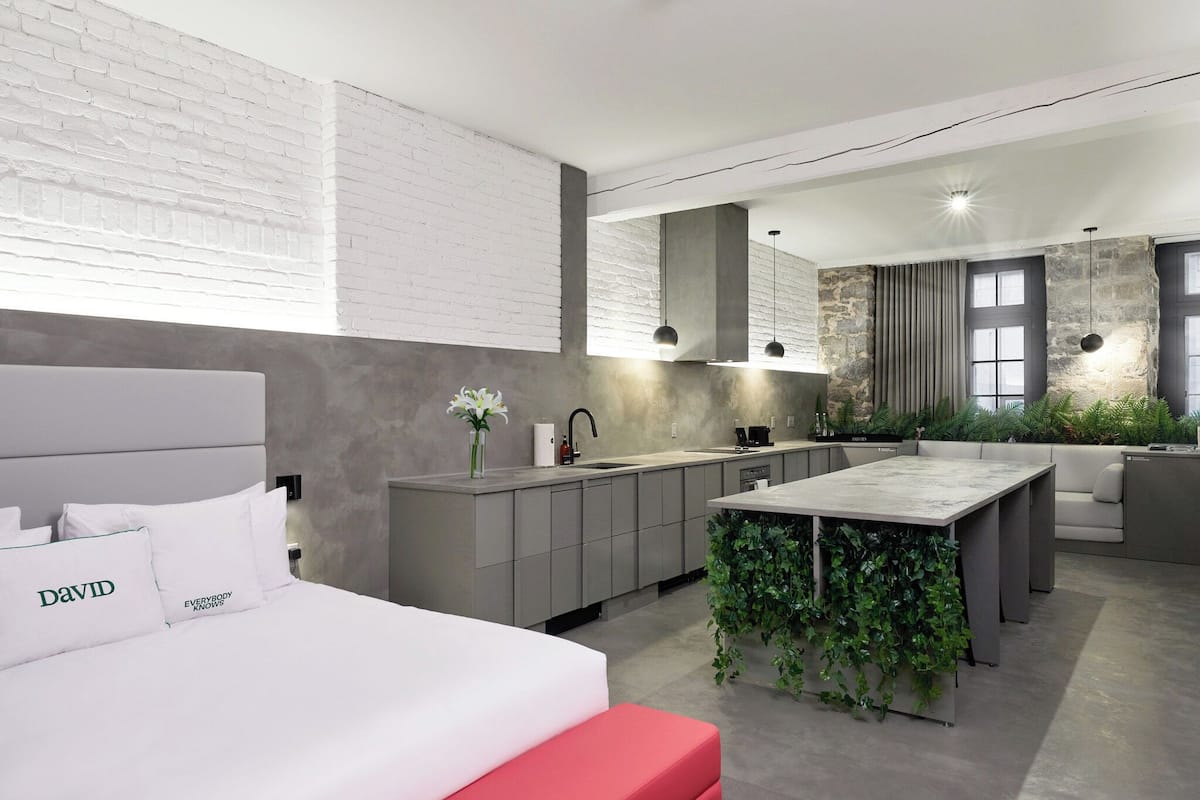 Una habitación de hotel moderna con una cama, un pequeño rincón con vegetación, una kitchenette y una zona de estar con sofá.