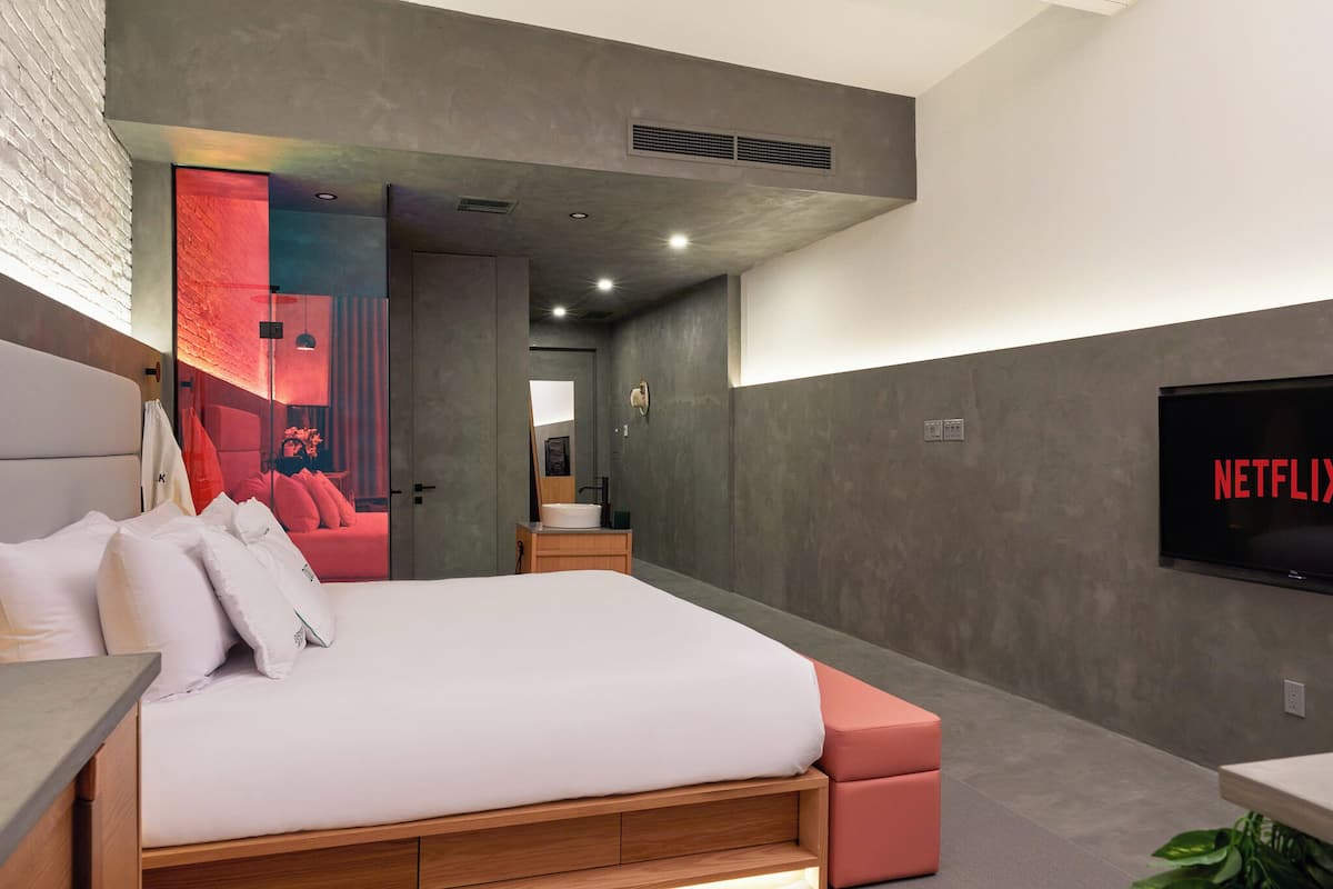 Una habitación de hotel moderna con una cama grande, un televisor montado en la pared y una pared decorada en rojo.