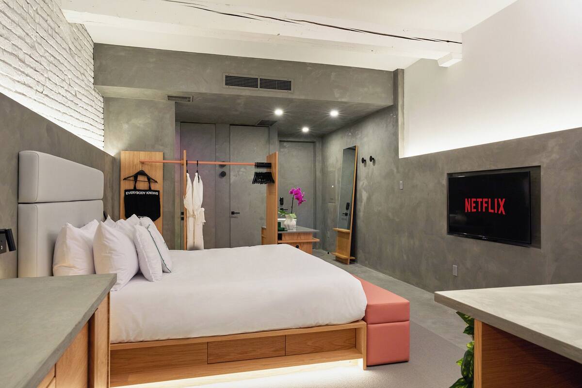 Un dormitorio moderno con una cama, un televisor que muestra 'NETFLIX' y un banco de madera.