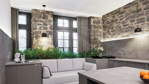 A modern kitchen with a stone accent wall, a built-in sofa, and a dining area with a bowl of fruit. - David Hotel (Montreal)