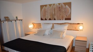 A neatly made bed with white linens and a black throw, two bedside tables with wall-mounted lamps, and a large leaf-patterned artwork above the bed. - GITES LE BRETZEL (Bergheim)