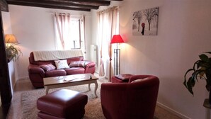 A living room with a red sofa, a coffee table, and a red armchair. There is a floor lamp and a painting on the wall. - GITES LE BRETZEL (Bergheim)