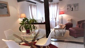 A dining area with a glass table, white chairs, a red rug, and a potted plant. - GITES LE BRETZEL (Bergheim)