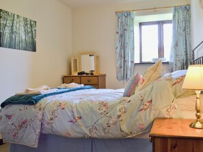 A bedroom with a bed, a dresser, a mirror, a window with curtains, and a lamp.