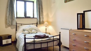 Un dormitorio con cama, mesita de noche con lámpara, cómoda y ventana con cortinas.