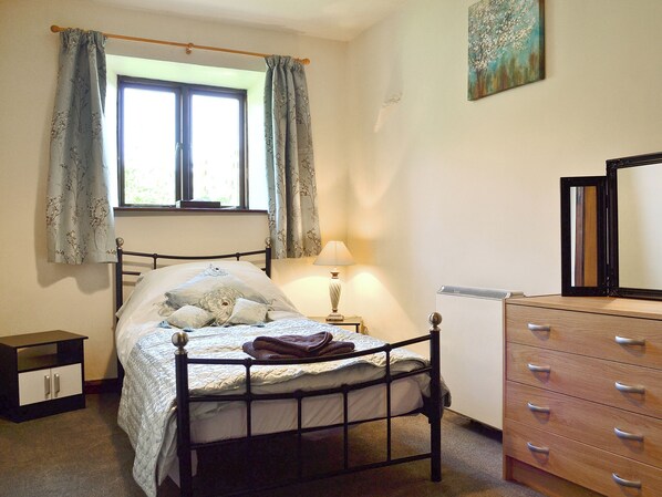 A bedroom with a bed, a bedside table with a lamp, a dresser, and a window with curtains.