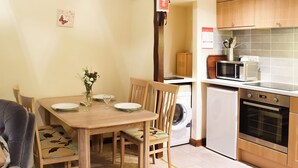 Una cocina compacta con zona de comedor, que incluye una mesa dispuesta para cuatro personas, lavadora, microondas y horno.