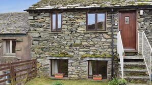 Una casa de piedra con puerta de madera, dos ventanas y un pequeño porche con macetas de flores.