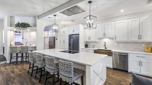 A modern kitchen with white cabinetry, a central island with bar stools, stainless steel appliances, and pendant lighting. - Lakefront-April Sound -Hot tub bath with Panoramic lake view- Fish off the dock (Montgomery)