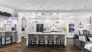 A modern kitchen with white cabinets, a central island with bar stools, and a dining area with a sofa and chairs. - Lakefront-April Sound -Hot tub bath with Panoramic lake view- Fish off the dock (Montgomery)