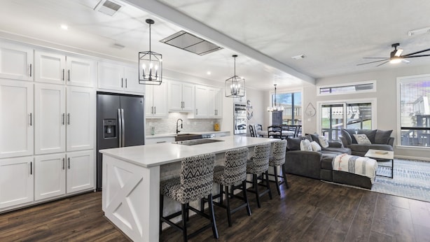 A spacious kitchen with white cabinetry, a large island with bar stools, and a dark wood floor. - Lakefront-April Sound -Hot tub bath with Panoramic lake view- Fish off the dock (Montgomery)