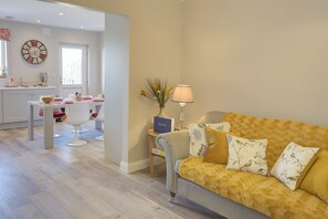 Ein modernes Wohnzimmer mit einer Couch, einem Esstisch und einer Küchenzeile im Hintergrund.