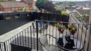 Un balcon avec une table et des chaises, des plantes en pot et une vue sur le quartier environnant.