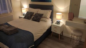 Une chambre à coucher bien rangée, avec un lit, des lampes de chevet, une table de chevet, un miroir et un petit tabouret.