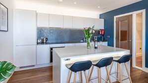 Una cocina moderna con armarios blancos, una isla central con taburetes y un jarrón con flores, además de una pared azul de acento.