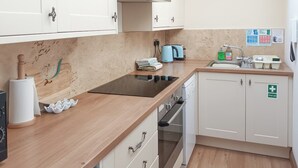 Una cuina moderna amb armaris blancs, forn integrat, rentapesos i un senyal de primers auxilis.
