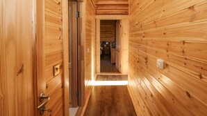 Un couloir en bois, avec une porte sur la gauche et une vue sur une pièce au fond.