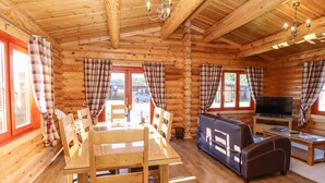 L’intérieur d’une cabane en rondins, avec une table à manger, des chaises, un canapé, un téléviseur et une cheminée.