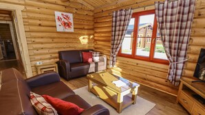 Et hyggeligt interiør i en træhytte med en lædersofa, et glasbord og ternede gardiner.