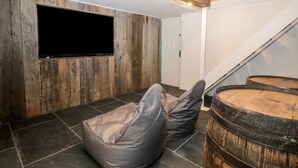 Una habitación con pared de madera, un televisor de pantalla plana montado, suelo de piedra y un barril de madera.
