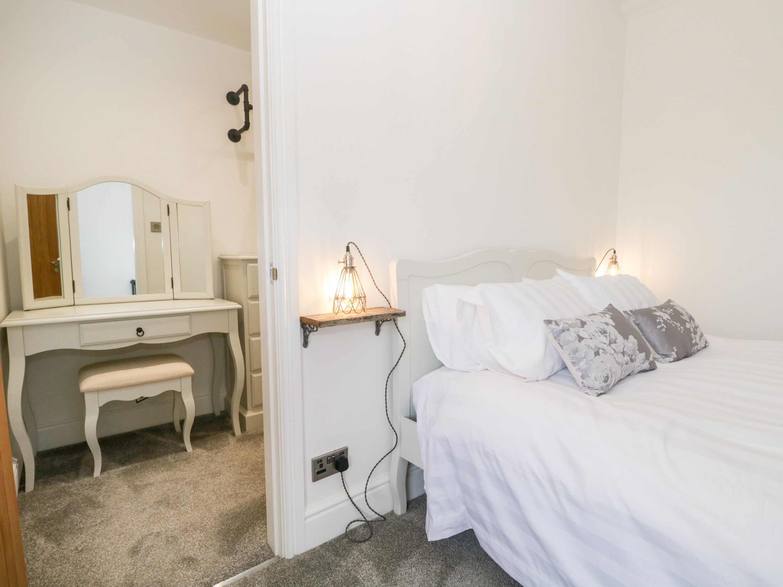 A bedroom with a bed, bedside lamps, a dresser, and a mirror.