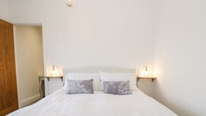Una cama bien hecha con sábanas blancas y dos almohadas, con lámparas de pared a cada lado.