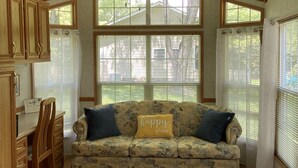 A cozy living room with a floral sofa, wooden cabinets, and large windows. - Tiny Toot - “On Deep Creek” Bryson City, NC  (Bryson City)