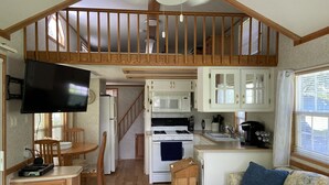 A cozy interior with a dining area, kitchen, and living space, featuring wooden beams, a TV, and a couch with a floral cover. - Tiny Toot - “On Deep Creek” Bryson City, NC  (Bryson City)