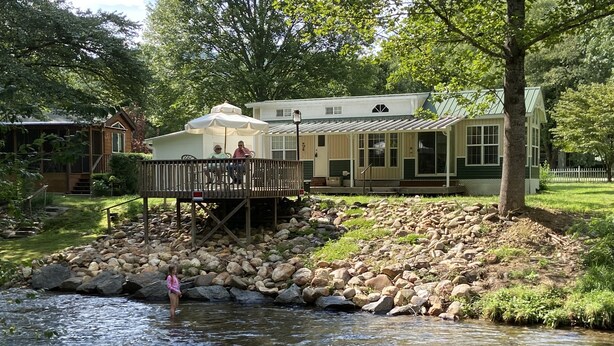 A riverside setting with a wooden deck and a building in the background. - Tiny Toot - “On Deep Creek” Bryson City, NC  (Bryson City)